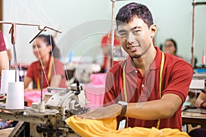 man smiling while sewing on a sewing machine at a clothing facto