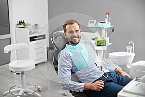 Man is smiling to the camera while sitting in a dental chair in dentistry being happy and satisfied with his treatment.