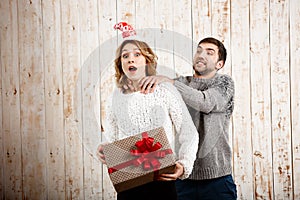 Man smothering girl holding christmas gift over wooden background.