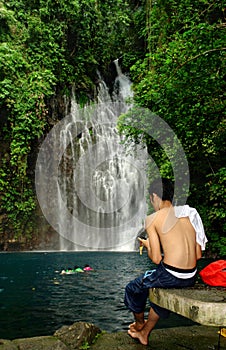 Man SMS-ing near tropical waterfall.