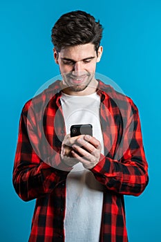 Man sms texting using app on smartphone. Handsome young guy surfing internet with mobile phone. Blue studio background