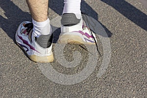 A man in sneakers with an untied lace walks down the street. Men's feet in shoes walking along the sidewalk