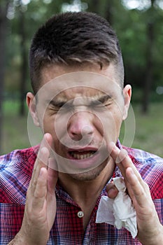 Man sneezing into Tissue. Handsome man blowing his nose in the park