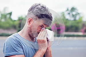 Man sneezing in a tissue outdoors. Pollen allergy, Springtime.