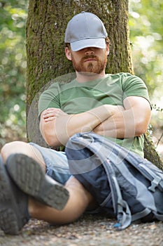 man snoozing against tree trunk