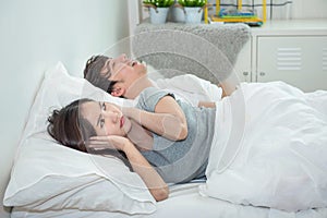 Man snoring while his wife is covering ears with the pillow.Asian young woman cover ears with pillow while her boyfriend sleep