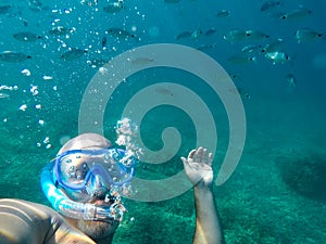 A man snorkling under the water with bubbles and lot of fish