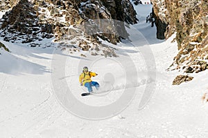 A man a snowboarder freerider descends a backcountry at high speed from a slope