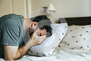 man sobbing into a pillow on his bed