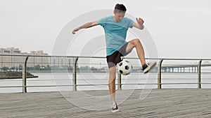 Man soccer player is kicking bouncing a ball performing tricks on waterfront.
