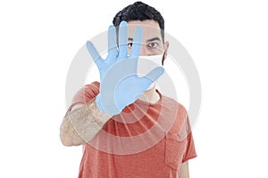 Man social distancing from corona virus wearing a protective white face mask and medical gloves holding up hand saying stop.