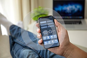 Man on sofa holding phone with app smart home screen