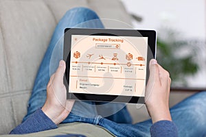 Man on sofa holding tablet app package tracking on screen