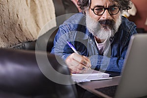 Man on a sofa with a laptop at home. Hipster make note while studying online watching webinar podcast on laptop listening