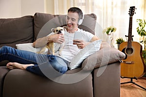 Man on sofa listening music with dog in his arms