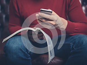 Man on sofa reading booklet and using smartphone