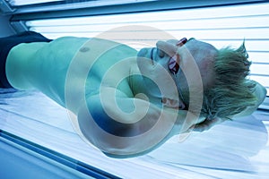 Man in solarium enjoying sunbathing on tanning bed