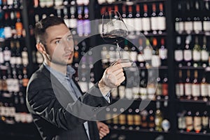 Man sommelier is holding glass of wine and tasting transparency light sediments in restaurant