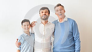Man, Son And Elderly Father Embracing Standing Over White Wall