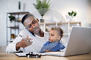 Man with son on knees working on laptop at home