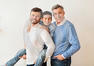 Man With Son And Senior Father Posing Near White Wall