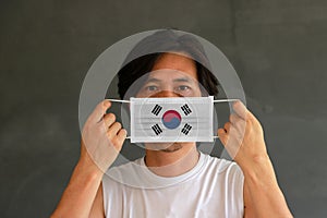 A man with South Korea flag on hygienic mask in his hand and lifted up the front face on dark grey background. Tiny Particle or