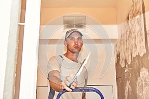 A man with a spatula is preparing to putty the surface of the wall to fix the walls and prepare for painting.