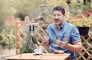 Man speaking in front of camera with attached mic lavalier. Vlogger man sitting on a table and making a vlog episode photo