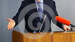 Man speaks in front of microphones, gesturing and standing behind a podium or pulpit. Lawyer, politician, businessman or teacher.