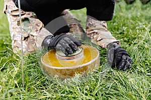 A man in a special suit works with a detector and found an explosive device. A man tries to neutralize an anti-tank mine