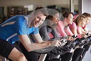 Man in a spinning class at a gym turning to smile at camera