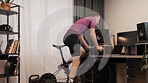 Man is spinning pedals on indoor smart bicycle trainer. Male cyclist is training at home during coronavirus lockdown. Professional