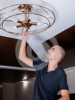 A man spins an LED lamp into a ceiling chandelier