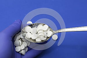 A man with a spoon pours pills into the palm of his hand in blue medical gloves concept medicine medicines pharmaceuticals
