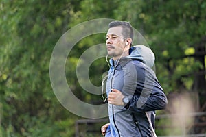 A man in sport hoodie jogging in the city park in the evening after stressful work
