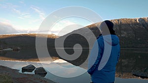 A man in sports clothes, looking at a beautiful reflection of the mountain peaks in the lake. Panorama.