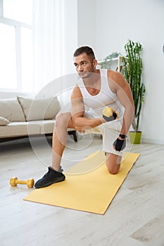 Man sports home training on the floor on a mat with dumbbells, exercises for muscle growth, pumped up man fitness