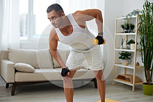 Man sports home training on the floor on a mat with dumbbells, exercises for muscle growth, pumped up man fitness