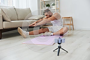 Man sports, watching a workout tape on his phone and repeating exercises blogger, pumped up man fitness trainer works