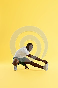 Man in sportswear stretching leg warming up on yellow background