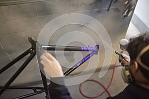 Man spray painting a bike frame in his workshop applying a protective clear coat