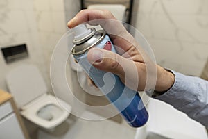 man spraying air freshener in bathroom. toilet spray in a man's hand on the background of toilet bowl