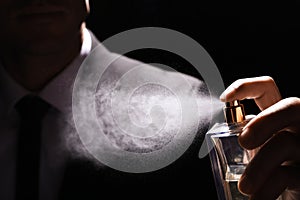 Man spraying luxury perfume on black background, closeup