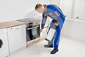 Man Spraying Pesticide In Kitchen Room