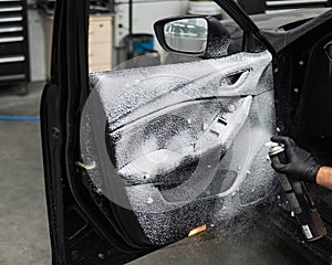 A man sprays cleaning foam on the interior of a car.