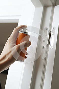 man sprays some lubricating oil on the hinge of a door