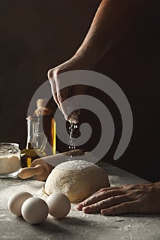 Man sprinkle flour on dough against dark background