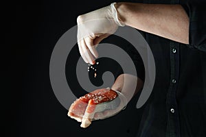 Man sprinkle salt on salmon meat on dark background