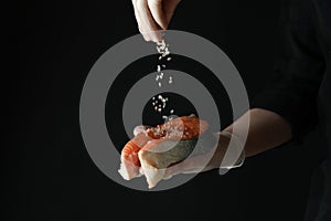 Man sprinkle salt on salmon meat on dark background