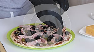 A man sprinkles oregano onto a pizza base. Cooking ingredients are laid out on it. Making pizza at home. Close-up shot